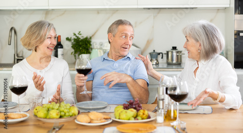 Happy pensioners gathered at the festive table - talking, discussing news and drinking red wine