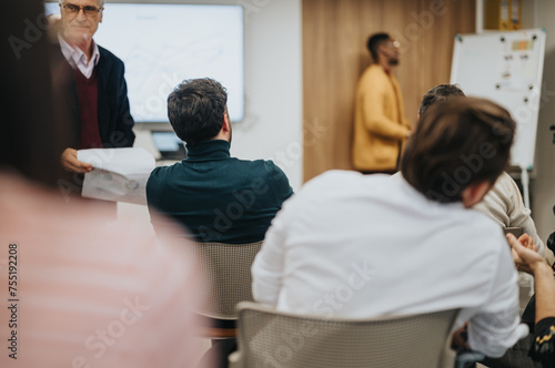 Focused group of professionals attending a business meeting with a speaker presenting. The setting is a contemporary office environment.