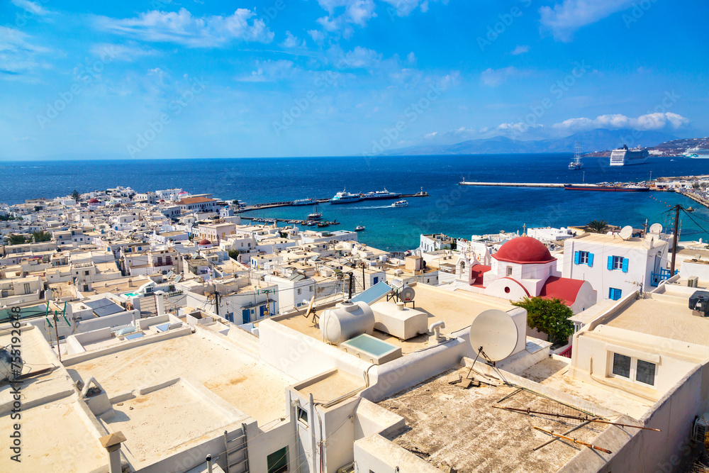 Chora port of Mykonos island with red church, famous windmills, ships and yachts during summer sunny day. Aegean sea, Greece