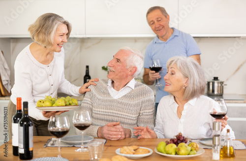 Couples of elderly women and men chatting and drinking wine at table..
