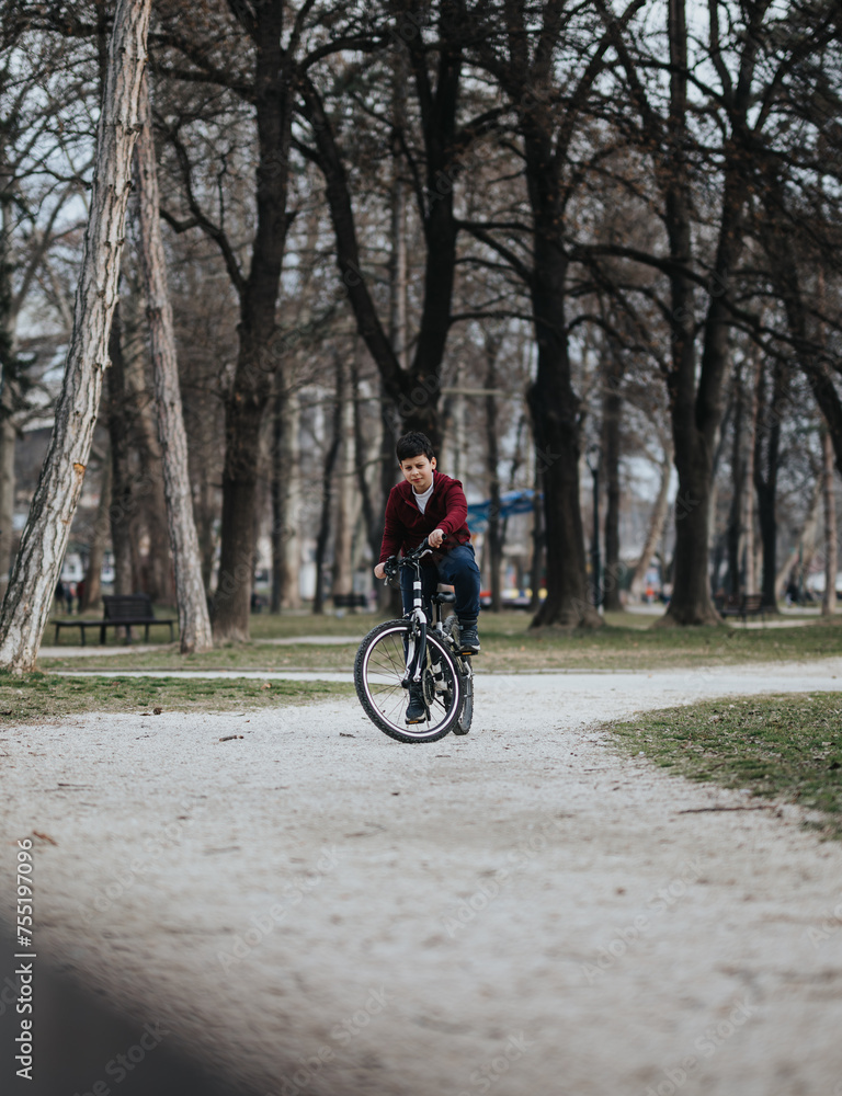 A boy rides his bicycle leisurely on a path in a city park, surrounded by nature and greenery.