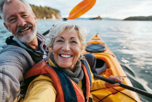 An elated senior couple shares a selfie moment while kayaking on serene waters, with smiles that reflect a deep bond and a zest for life.