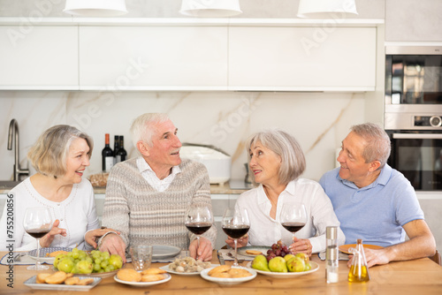 Couples of elderly women and men chatting and drinking wine at table..