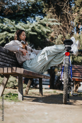 A serene moment captured as a young woman lounges on a park bench with her bicycle beside her, embodying leisure and tranquility.