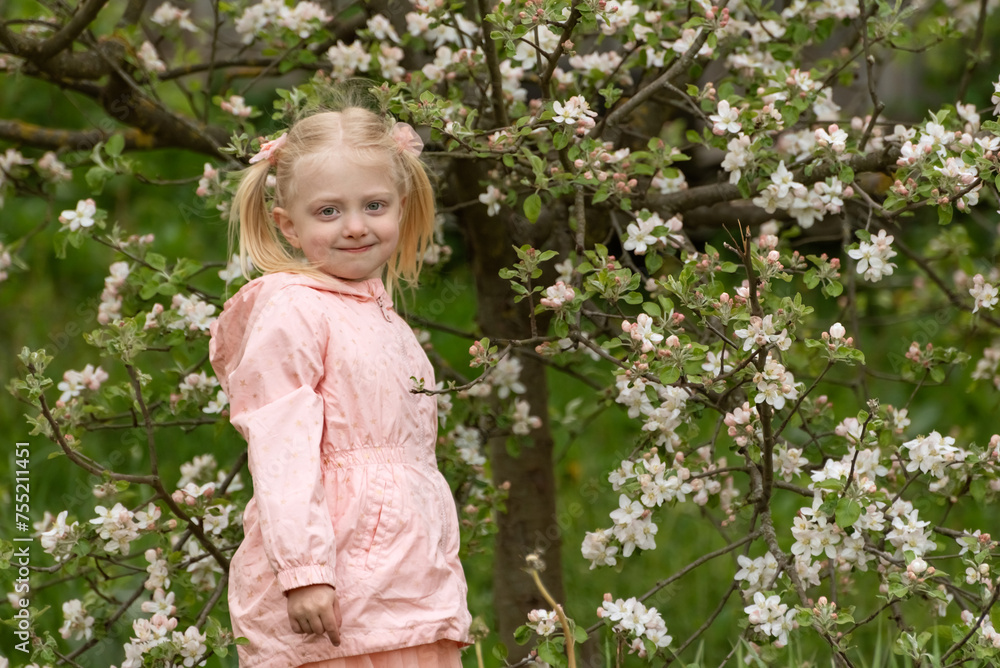 Portrait of cute beautiful blonde girl with two ponytails wears pink jacket stands in spring garden near flowering tree. Portrait of cute beautiful blonde girl with two ponytails wears pink jacket stands in spring garden near flowering tree.