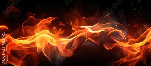 A close-up view of fiery flames dancing and flickering intensely on a stark black background. The vibrant orange and yellow colors of the fire create a striking contrast against the darkness.