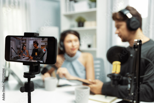 Focus on smartphone recording with blurry host channel broadcasters background making advice problem in live streaming with listeners with set live on talking show radio at modern studio. Postulate.