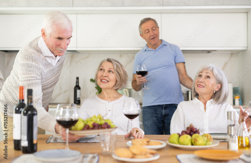 Couples of elderly women and men talking and drinking wine in kitchen