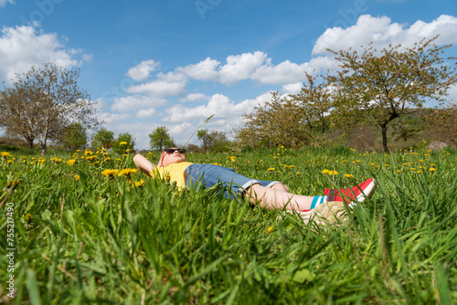 Child boy lies in grass in dandelions field and rejoices in sun. Summer vacation in the countryside.
