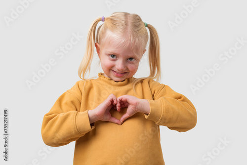 Lovely little girl with blond hair making a heart shape with her hands, looking at camera, isolated over white background