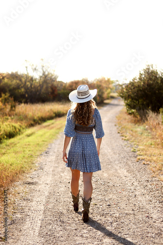 Girl with Cowboy Hat Walking Down Dirt Road © Micah