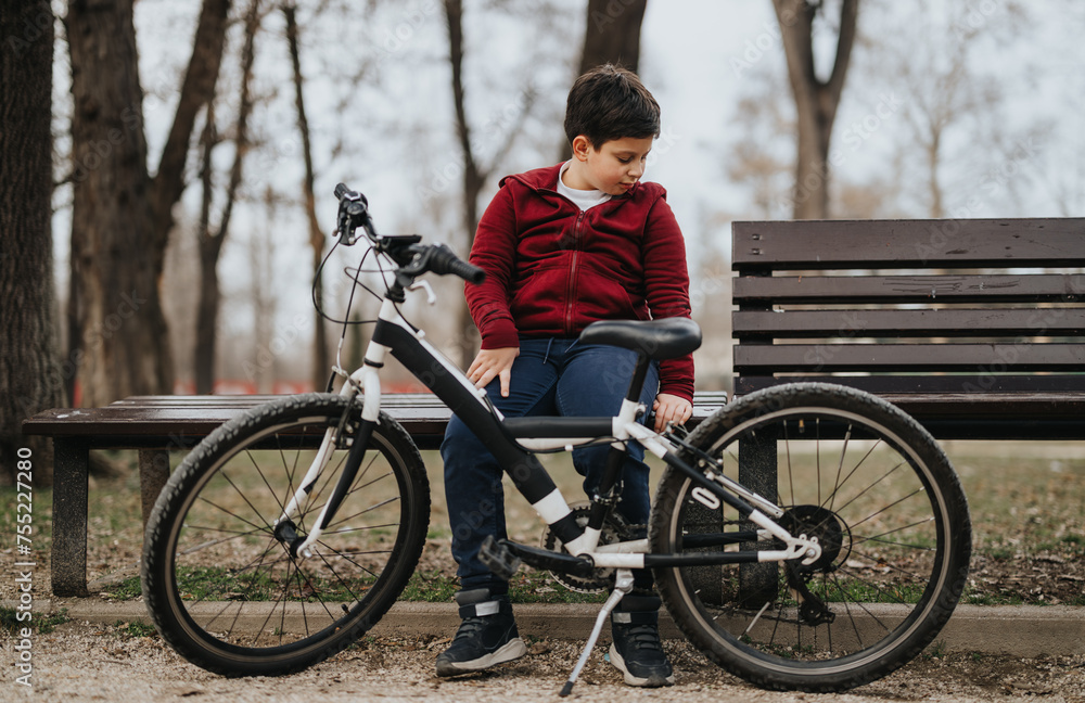 A contemplative young individual rests on a bench beside a bicycle, surrounded by the tranquility of a leafy park.