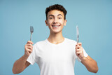 Smiling attractive boy holding fork and knife looking at camera. Hungry teenager