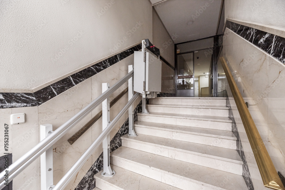 Access portal to a residential apartment building with marble-clad walls, railings with metal handrails and a wheelchair lift