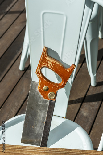 a manual woodworking saw with a wooden handle resting on the back of a metal chair