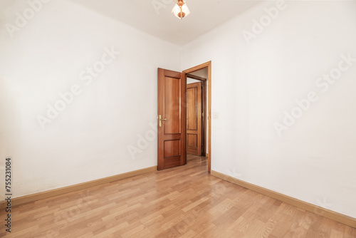 An empty room with white painted walls, wooden floor and sapelly door in a corner