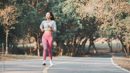 Full body female athlete in activewear running on road path during cardio workout on sunny summer day in park.