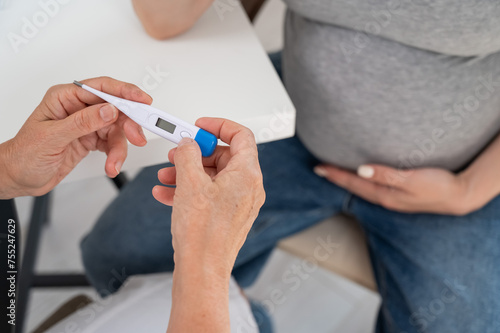 A pregnant woman visits a doctor. Therapist holding an electronic thermometer. 