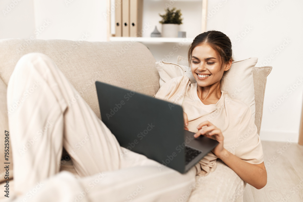Smiling Woman Freelancing on a Laptop at Home: Modern Lifestyle and Technology in a Cozy Living Room Smiling Woman Freelancing on a Laptop at Home: Modern Lifestyle and Technology in a Cozy Living Room