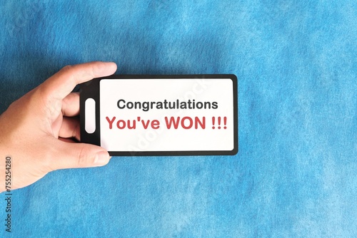 Winning text scam concept. Hand holding mobile phone with congratulatory message in blue background.