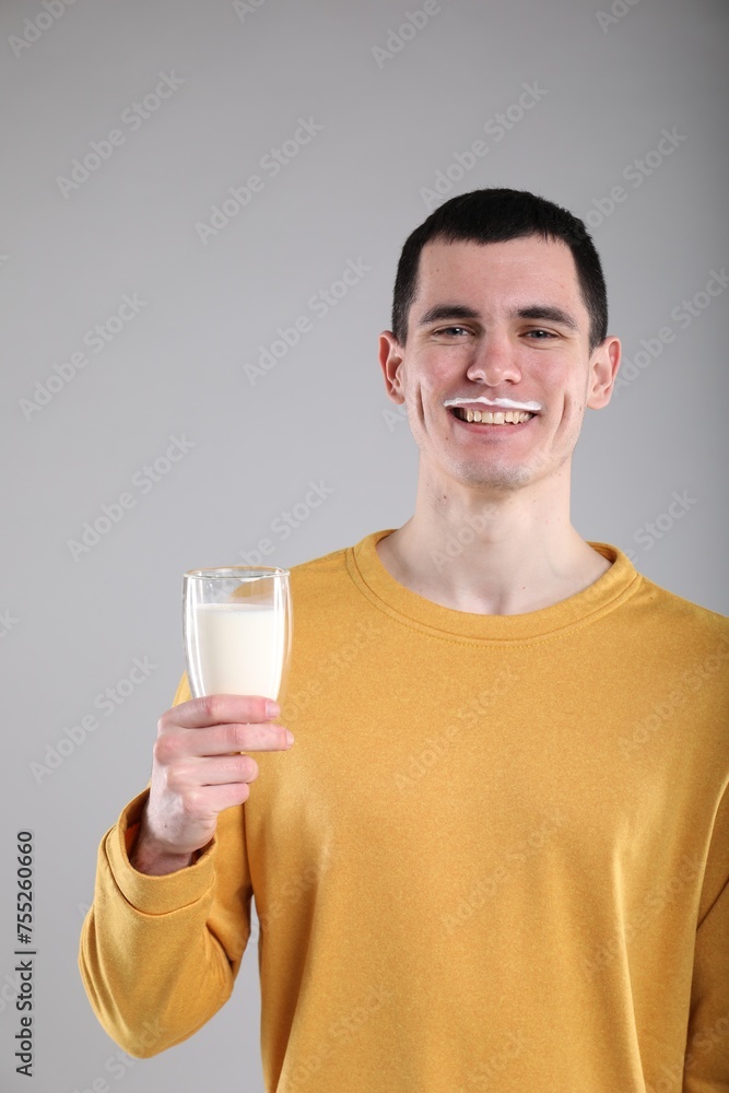 Happy man with milk mustache holding glass of tasty dairy drink on gray background Happy man with milk mustache holding glass of tasty dairy drink on gray background
