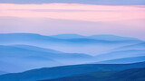 Layers of blue mountains and hills shrouded in mist under a soft pink and blue gradient sky at twilight