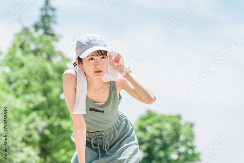 公園でランニング・ジョギング中にタオルで汗を拭く若いアジア人女性 
