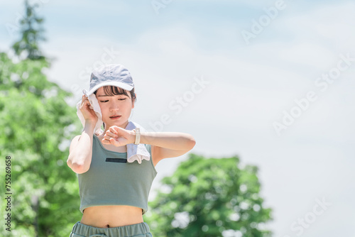 公園でトレーニング・ジョギングのインターバル中にスマートウォッチを確認する若いアジア人女性 