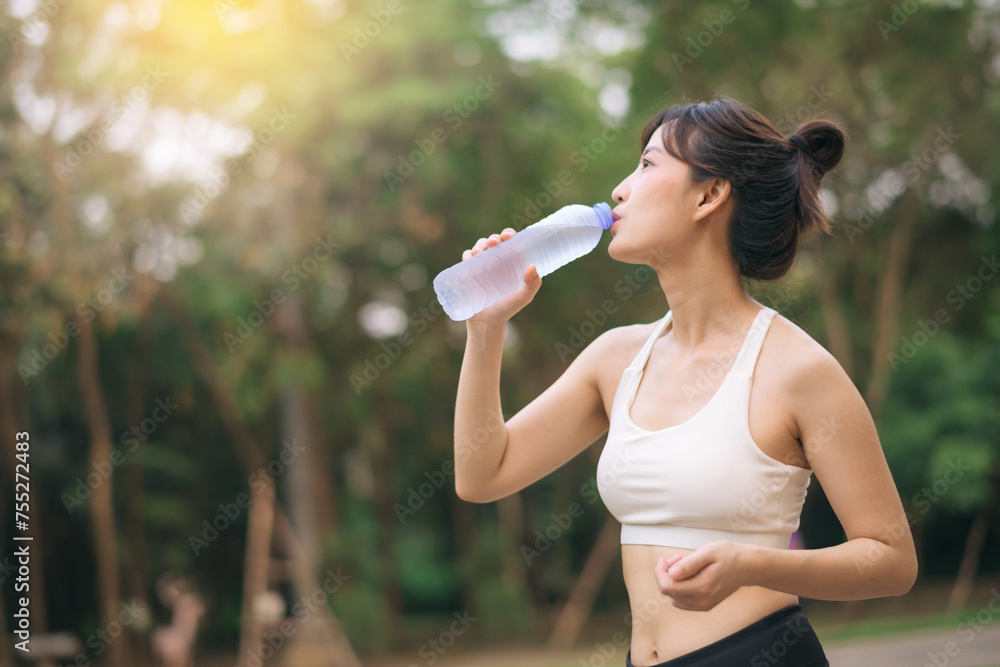 Female runner. Fit Asian young woman with white sportswear drinking water after running and enjoying a healthy outdoor. Fitness runner girl in public park. Wellness being concept Female runner. Fit Asian young woman with white sportswear drinking water after running and enjoying a healthy outdoor. Fitness runner girl in public park. Wellness being concept