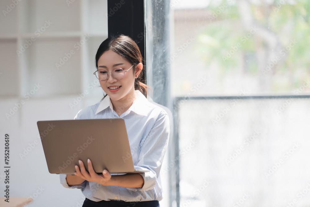Cheerful Asian businesswoman with glasses working with laptop in her room. Cheerful Asian businesswoman with glasses working with laptop in her room.