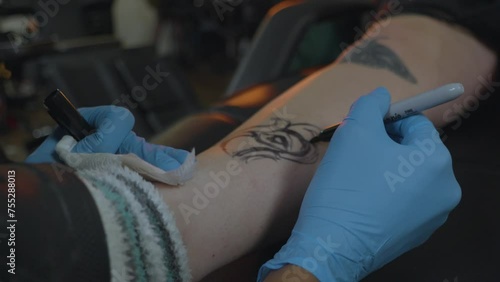 a tattoo artist sketches the pattern for a rose tattoo onto the clients leg in preparation for ink photo