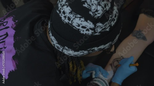 a tattoo artist with dreadlocks sketches a rose pattern onto the leg of his client before applying ink photo