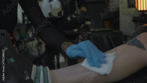 a woman in a tattoo shop sterilizes the leg of a client in preparation of inking a tattoo onto her skin photo