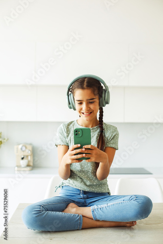 Cute nine year old girl wearing headphones holding a smartphone and taking a selfie, childhood and technology concept.