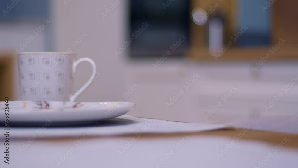 Hand holding cup of coffee hovers above plate on wooden table Hand holding cup of coffee hovers above plate on wooden table