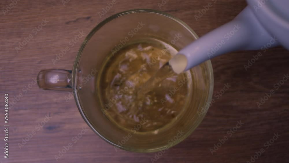 Pouring tea into a glass cup on a wooden table made of hardwood Pouring tea into a glass cup on a wooden table made of hardwood