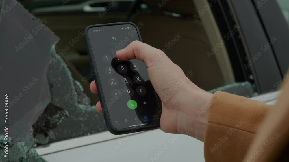 Man holds a mobile phone in front of the broken car window, dials the emergency number to make a call. The owner calls the police after discovering the broken window of his car. Man holds a mobile phone in front of the broken car window, dials the emergency number to make a call. The owner calls the police after discovering the broken window of his car.
