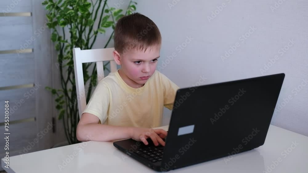 teenage boy studies or plays game on laptop against background of home interior. Concept of working and playing on computer. Children's time outside of school teenage boy studies or plays game on laptop against background of home interior. Concept of working and playing on computer. Children's time outside of school