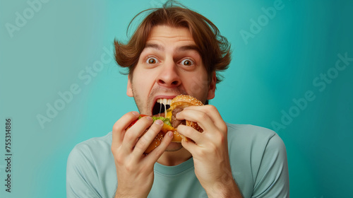 Portrait Of Funny Hungry Guy Holding Biting Burger Eating Junk Food Posing With Open Mouth Over teal Studio Background  Enjoying Unhealthy Nutrition.Binge Eating Habit Concept professional photography