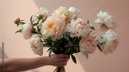 Fototapeta Naklejka Na Ścianę i Meble -  hand holding a bouquet of peonies against a light wall