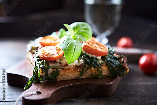 Open-faced toasted cheese sandwich with cherry tomatoes, spinach and fresh basil. Brown wooden background.