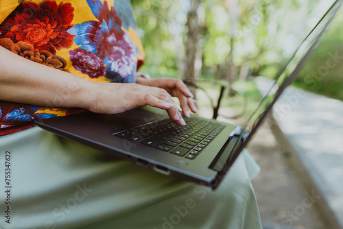 Office outdoors, close-up of female hands typing on a keyboard with a laptop in nature. Nature meets technology: woman using her laptop outdoors on a sunny day, hands close-up.