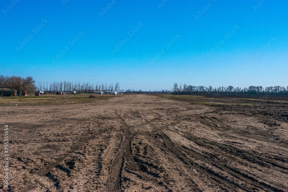 the runway of a rural field aviation airfield, slightly damaged after winter rains, on a sunny winter day