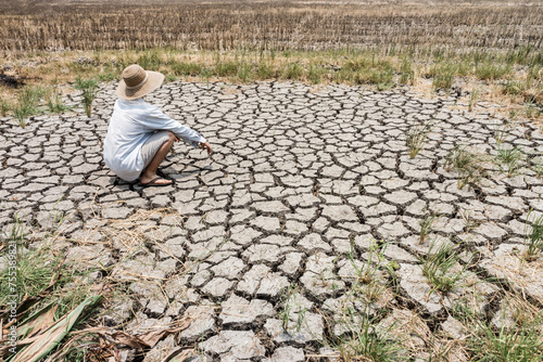 A poor farmer squatting and watching the barren agricultural field. The cause is a lack of water during the long dry season which is caused by the phenomenon of global warming.
