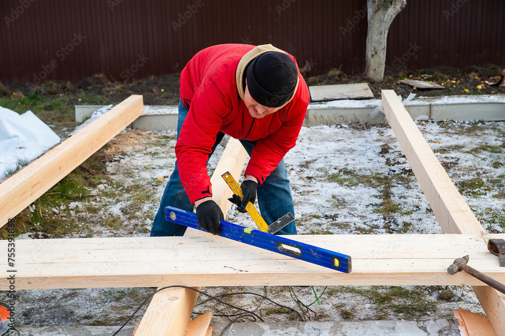 A man in a red jacket is engaged in construction using wooden planks. Measures level A man in a red jacket is engaged in construction using wooden planks. Measures level