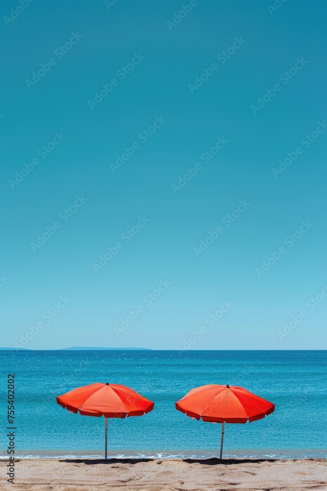 Two red beach umbrellas on a sunny day with clear skies.