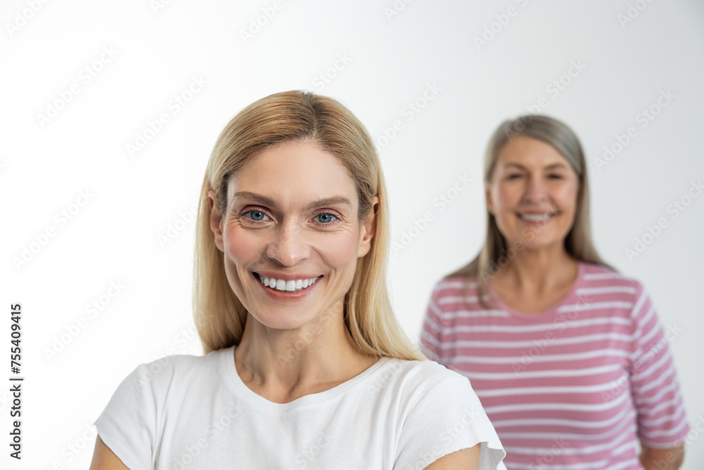 Blonde cute woman smiling nicely, her mom standing behind Blonde cute woman smiling nicely, her mom standing behind