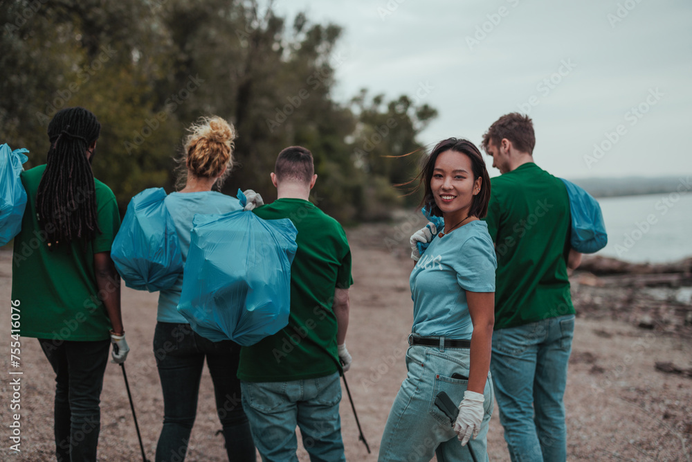 Female volunteer collecting trash smiles for the camera as his colleagues collect