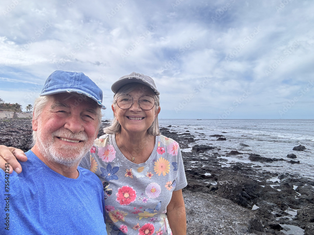 Happy smiling senior couple in retirement enjoying a day at sea while taking self portraits together with a smartphone