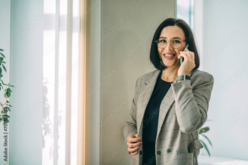 Smiling businesswoman using her phone in the office. Small business entrepreneur talking on mobile phone and smiling while communicating in office Smiling businesswoman using her phone in the office. Small business entrepreneur talking on mobile phone and smiling while communicating in office